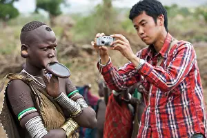 Rural Scene Prints: Japanese Tourist Taking A Picture Of A Slightly Annoyed Mursi Tribal Woman Wearing A Large Pottery Lip-Plate (Dhebi)
