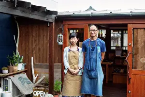 Leather Prints: Japanese woman and man wearing blue apron standing outside a leather shop