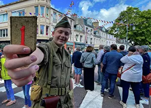 Strongertogether Prints: A kid from Carentan holds up a 1st Infantry Division patch during a D-Day commemoration parade at Carentan