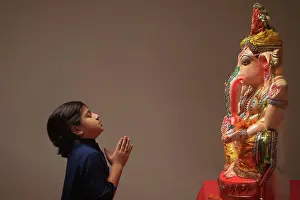 Occasion Prints: Kid praying with hands joined and eyes closed in front of Ganpati Idol
