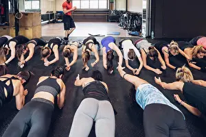 Instruction Prints: Large group of women training in gym with male trainer, doing push ups