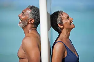 50 To 55 Years Prints: Laughing mature couple standing back to back on a beach
