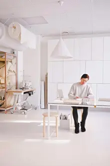 Place Of Work Prints: Full length of mature female design professional is writing in note pad at desk in workshop