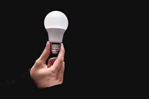 Consumption Prints: light bulb in hand on a black background