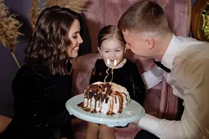 Father Prints: Little girl blows out the candles on the cake with her parents