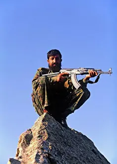 Dangerous Prints: A local Afghan fighter is perched atop the pinnacle of a rock as he scans a suspected Al Qaeda training camp