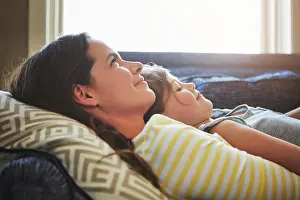 Cuddle Prints: Love, rest and mother cuddle her child while relaxing on sofa in the living room of their home