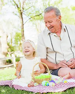 Grandfather Prints: Loving grandfather and granddaughter coloring easter eggs together on picnic blanket at the park