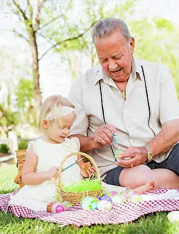 Loving grandfather and granddaughter coloring easter eggs together on picnic blanket at the park