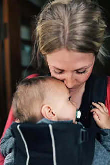 Verticals Prints: Loving mid adult mother carrying baby in carrier at home