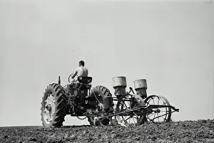 Full Length Prints: Low angle view of a farmer planting corn with a tractor in a field
