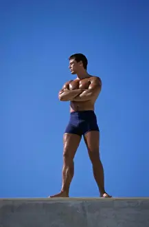 Macho Prints: Low angle view of a young man standing with his arms folded