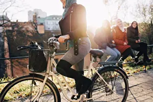 Muslim Prints: Low section of woman cycling by female friends sitting on railing in city