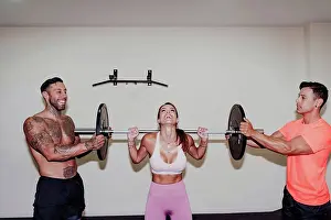 Small Group Prints: Male athletes helping female friend in exercising with barbell at gym