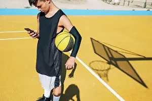 Game Prints: Male basketball player using his smartphone resting after training session
