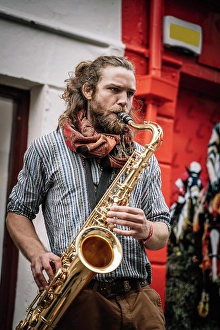 Expressive Prints: Male bearded and long haired saxophonist plays sax with bright emotions in the street