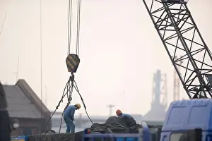 Thirty Prints: Two male construction workers hooking cables to a crane in a shipping yard