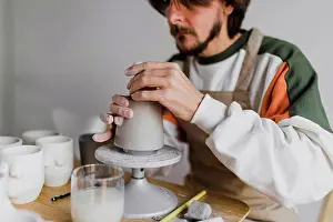 Competence Prints: Male expert molding clay on pottery wheel at workplace