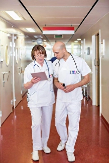 Mid Adultman Prints: Male and female doctors using digital tablet while walking in hospital corridor