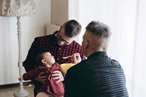 Dads Prints: Male gay couple with adopted baby girl at home - Two handsome dads feed the baby girl on kitchen - Male babysitters