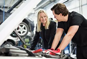 Communications Prints: Male mechanic discussing with female customer while repairing car engine at workshop