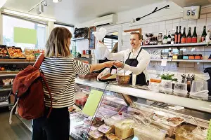Self Employed Prints: Male sales clerk holding plastic bag while accepting credit card from customer at checkout counter