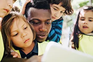 Midadult Men Prints: Male teacher sharing digital tablet with students in playground