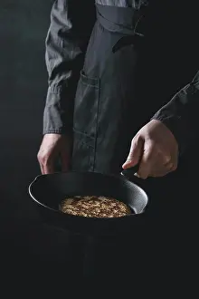 Back Ground Prints: Man chef in black apron cooking pancakes in cast-iron pan
