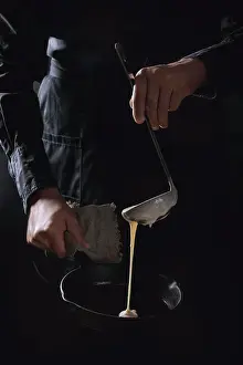Back Ground Prints: Man chef in black apron pouring dough from ladle for cooking pancakes in cast-iron pan