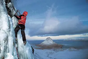 Glacier Prints: man climbs frozen waterfall above Grundafjordur fjord in Iceland