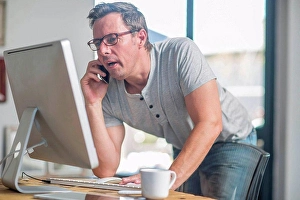 Consumer Electronics Prints: Man at computer using smartphone to make telephone call