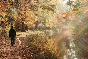 People In Nature Prints: Man and dog walking on canal towpath in fall with rainbow flare