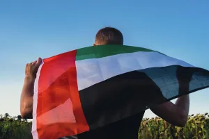 Staedtisch Prints: Man holding National Flag Of UAE Waving In The Wind sunset