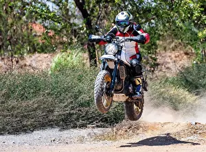 Dusty Prints: man jumping his scrambler type motorcycle on dirt track in Thailand