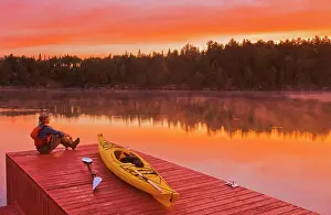 Paddle Prints: man next to kayak on on dock at sunrise, Lake of the Woods, Northwestern Ontario, Canada