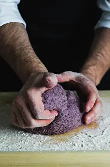 Flour Prints: A man kneading a purple bread dough on a floured wooden surface