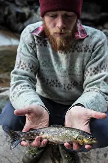 Sweater Prints: Man proudly displaying his catch by the river