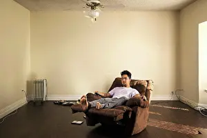 Home Prints: Man sitting in armchair watching television in barren apartment