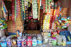 India Prints: Man in his small local shop selling piled up biscuits and sweets in rural town