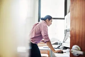Midadult Men Prints: A man standing in his office leaning on the desk, viewed through an open door