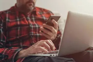 Self Employed Prints: Man using laptop and holding smartphone
