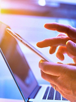 Consumer Electronics Prints: Man using a mobile phone with a laptop in the background