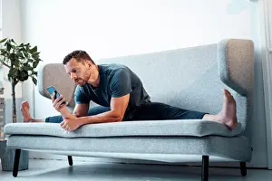 Typing Prints: Man using smart phone sitting with legs apart on sofa at home