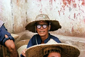 Weathered Prints: Man wearing a straw hat and black rimmed glasses sitting outside a building