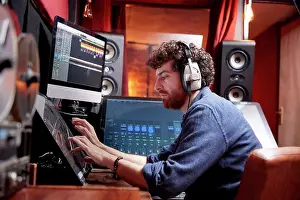 Electronics Prints: Man working in music studio using computer wearing head phones