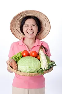 Only Women Prints: Mature farmer holding a sieve of vegetables, laughing