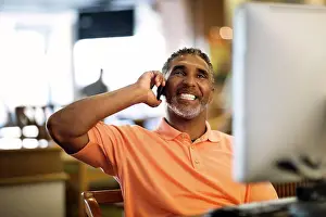 Conversation Prints: Mature man talking on his cell phone while working on a computer in an office in his home