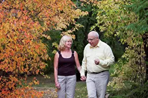 Baby Boomer Prints: Mature married couple walking together in park during fall season