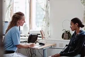 Communications Prints: Mature nurse explaining to female patient while sitting at doctor's office