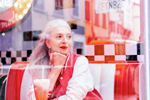 Deep Thought Prints: Mature woman in baseball jacket looking through window from 1950's diner